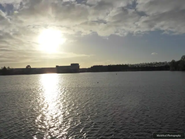 The low sun reflects across the lake beneath a cloudy evening sky.