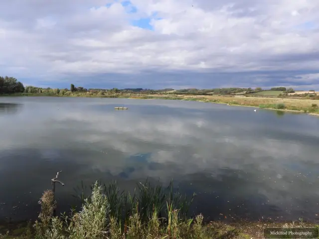Clouds and open countryside are reflected in the still water of the wetland.