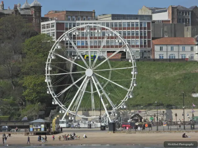 Scarborough's seafront wheel stands beside the beach, with the hillside buildings behind it.