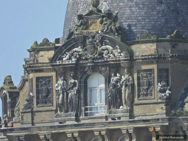 A close view of ornate stone figures and carvings above a window on the Grand Hotel.