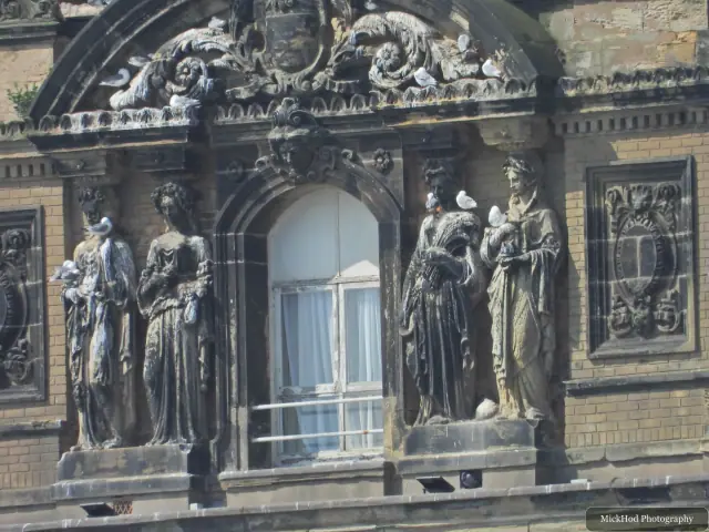 Weathered sculpted figures flank an arched window on the Grand Hotel façade.