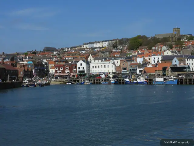 Colourful buildings climb the hillside above Scarborough Harbour, viewed across the water.