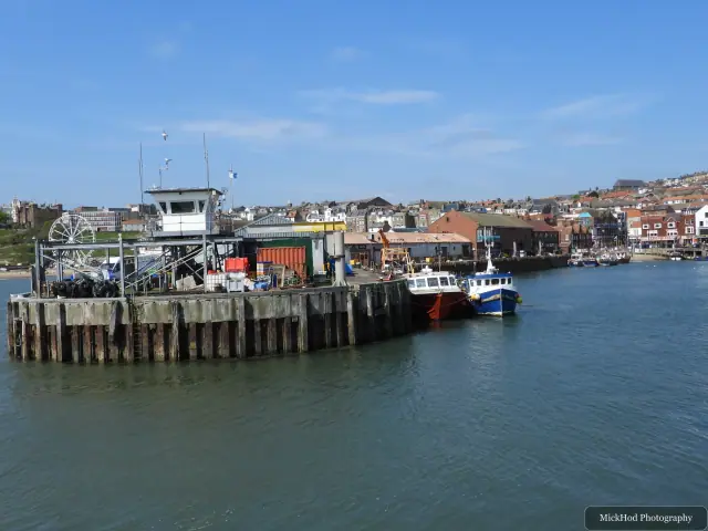 Boats gather beside the harbour pier, with the lighthouse visible at the end of the breakwater.