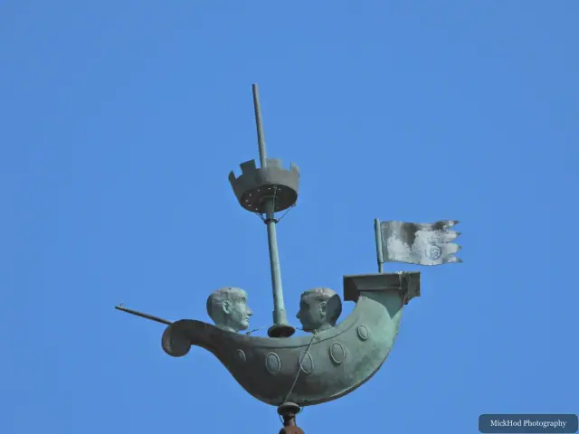 A bronze sculpture depicts two figures in a small boat against the open sky.