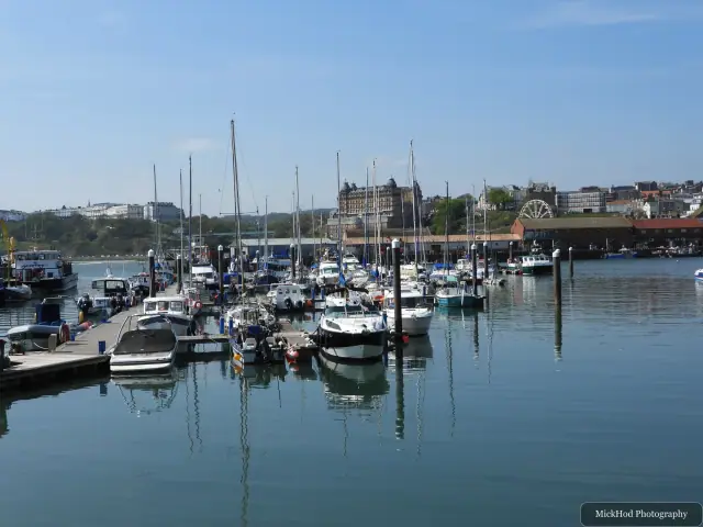 Small boats fill the harbour, with the Grand Hotel and green headland in the distance.