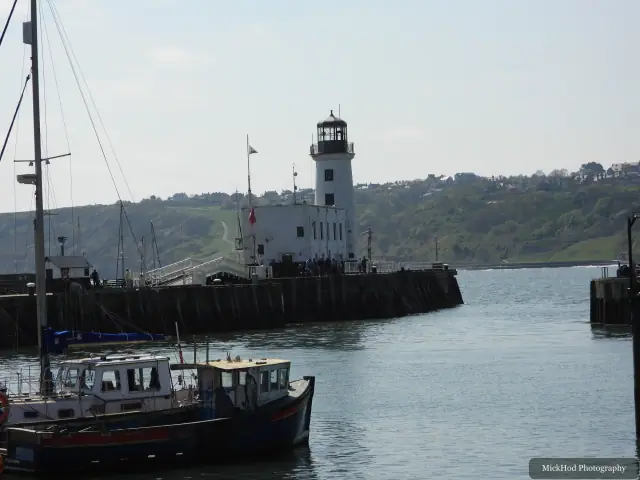 A white lighthouse stands at the end of the pier, with moored boats in the foreground.