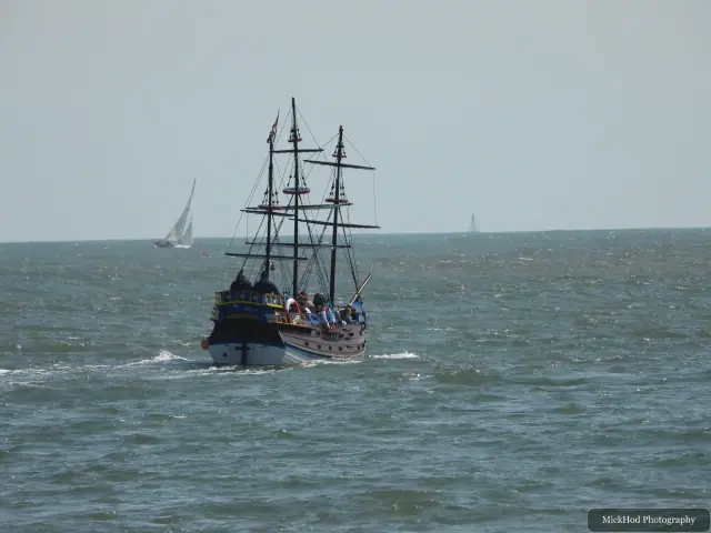 A tall-masted sailing ship moves across the open sea, with smaller sails on the horizon.
