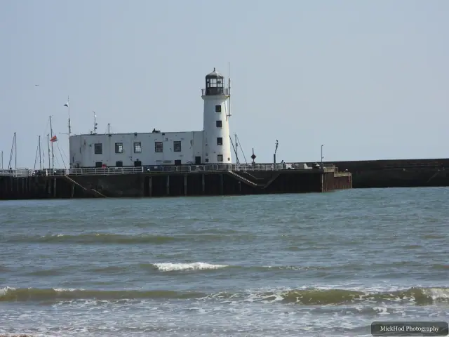 The white harbour lighthouse stands above waves breaking along the pier.